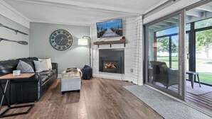 Una sala de estar moderna con chimenea, un reloj grande y un televisor montado encima.