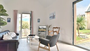 A modern living room with a sofa, a chair, a coffee table, and a television. There is a sliding glass door leading to a garden. - La Petite Jeanne (Cancale)