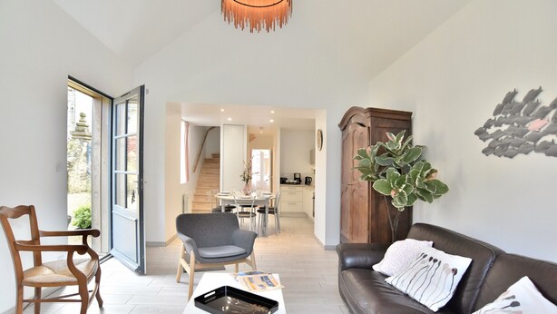 A modern living room with a leather sofa, a wooden chair, a dining area in the background, and a large plant. - La Petite Jeanne (Cancale)