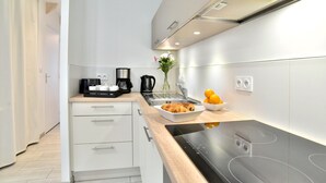 A modern kitchen with white cabinetry, a black induction cooktop, a sink, and a coffee maker. - La Petite Jeanne (Cancale)
