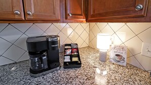 Une machine à café, un support pour dosettes de café et un paquet de café sur un plan de travail de cuisine, avec un dosseret carrelé et des placards en bois.