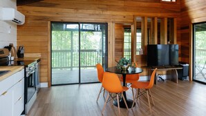 Une cuisine moderne avec un intérieur en bois, un coin repas avec des chaises orange et un téléviseur posé sur une table en bois.