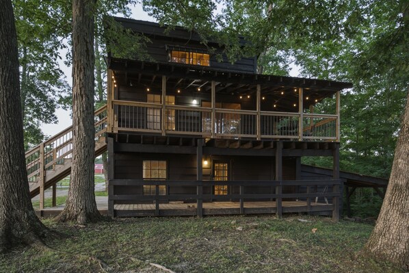 A multi-level wooden cabin with a balcony, surrounded by trees.