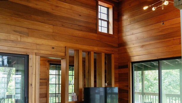 L’intérieur d’un chalet en bois comprend un coin repas avec des chaises orange, une table et un téléviseur.