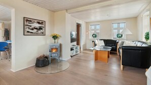 Un salon moderne avec un poêle à bois, un canapé en cuir noir, une table basse en verre et un coin repas avec des chaises bleues.