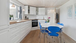 Une cuisine moderne avec des meubles blancs, un plan de travail en bois et un coin repas avec des chaises bleues.