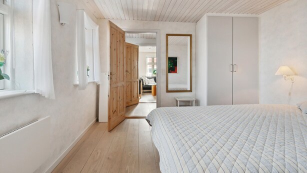 Une chambre à coucher avec un lit, une armoire, un miroir et une fenêtre avec des rideaux.