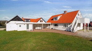 Une maison à deux étages, avec un toit recouvert de tuiles rouges, un patio abrité et une façade blanche.