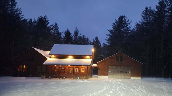 Een houten hut met een sneeuwbedekte dak en een garage, omringd door een bos.
