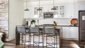 A modern kitchen with white cabinets, a stainless steel refrigerator, and a central island with bar stools. - Coastal Village Townhome | Blocks2 Grandview Beach (Encinitas)
