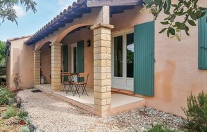 A house with a covered porch, a door with green shutters, and a small table with chairs.