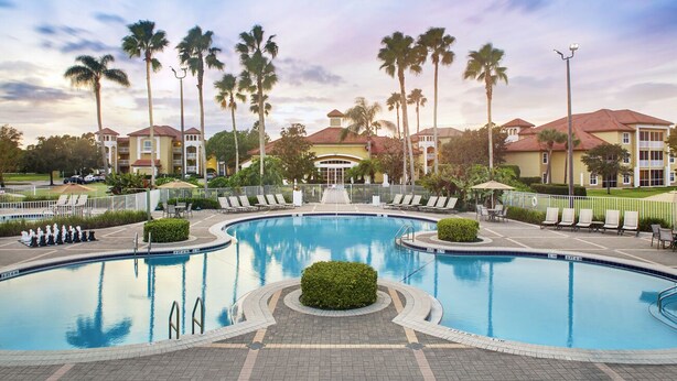 A swimming pool with lounge chairs and palm trees, surrounded by hotel buildings. - Cozy 1BR Villa at Sheraton PGA Resort Near Golf & Florida Attractions (Port St. Lucie)
