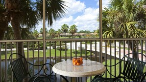 A balcony with a round table and two chairs, overlooking a well-maintained garden with palm trees and a pond. - Cozy 1BR Villa at Sheraton PGA Resort Near Golf & Florida Attractions (Port St. Lucie)