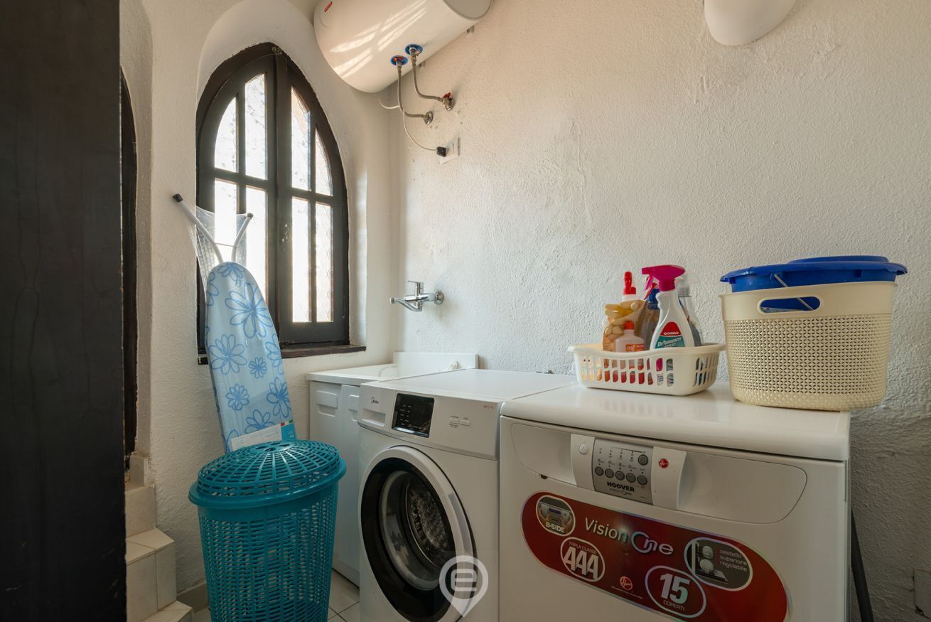 A laundry area with a washing machine, dryer, ironing board, and laundry baskets.
