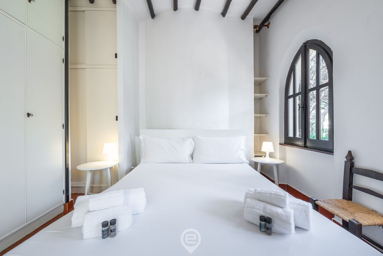 A hotel room with a large bed, two bedside tables with lamps, a window with a view, and a wardrobe.
