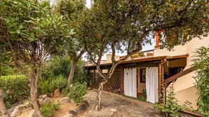 A stone pathway leading to a building with a wooden deck and a covered entrance. - Villa Mirto – Cozy Cottage with Garden and Terrace (Is Molas)