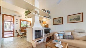 A living room with a fireplace, sofa, coffee table, and shelves with decorative items. - Villa Mirto – Cozy Cottage with Garden and Terrace (Is Molas)