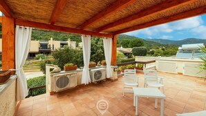 A covered outdoor patio with a view of the surrounding landscape, including a mountain and greenery. - Villa Mirto – Cozy Cottage with Garden and Terrace (Is Molas)