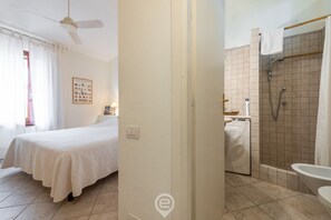 Un dormitorio con cama, ventilador de techo y baño privado con ducha, inodoro y lavamanos.