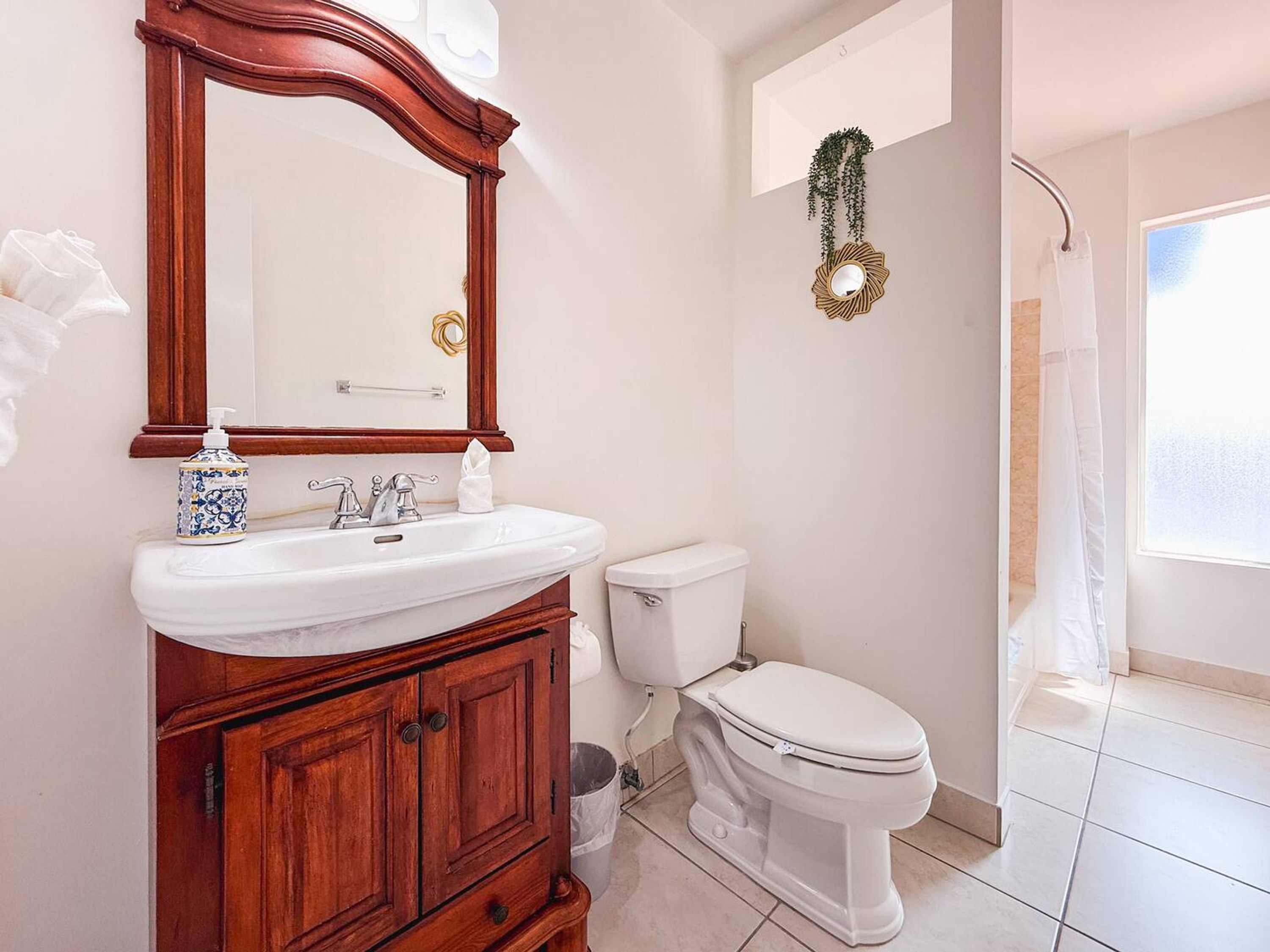 A bathroom with a wooden vanity, white sink, and toilet. There is a mirror above the sink and a shower curtain visible in the background.