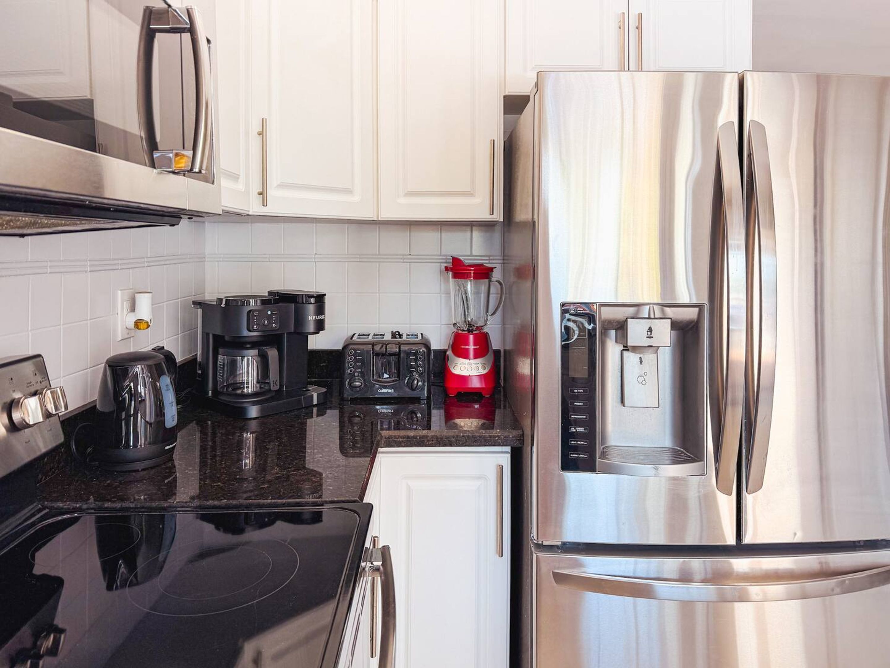 A modern kitchen with white cabinets, a stainless steel refrigerator, a coffee maker, a toaster, and a blender.