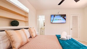 A bedroom with a bed, pillows, a blue towel, a painting of a beach, and a ceiling fan. - Waterfront Florida Vibes and Views - King Bed (Fort Lauderdale)