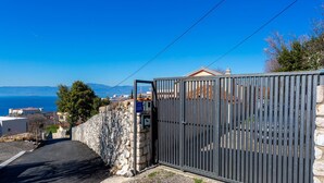 A gated property with a stone wall, a metal gate, and a view of the sea and mountains in the background. - Cozy apartment in Kraljevica with house sea view (Kraljevica)