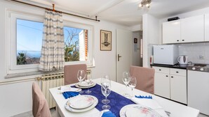 A dining area with a table set for four, a window with curtains, a kitchen with white cabinets, and a radiator. - Cozy apartment in Kraljevica with house sea view (Kraljevica)