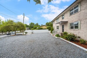 A residential building with a gravel driveway, a white fence, and a small porch with steps.