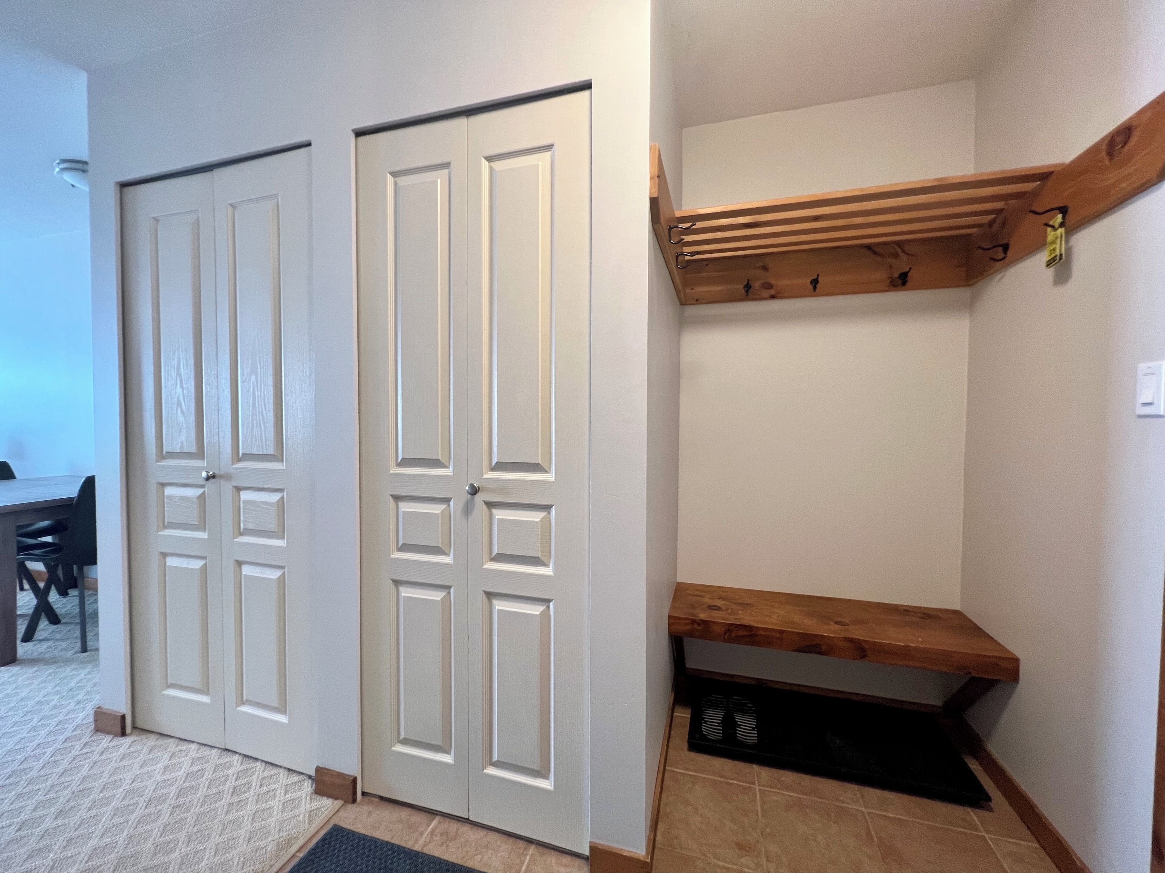 A hallway with two white doors, a wooden bench, and a small shelf.