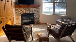 Una sala de estar acogedora con chimenea de piedra, un televisor y dos sillones de cuero.