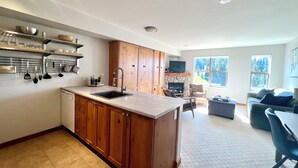 Una cocina moderna con armarios de madera, un lavamanos integrado y una chimenea de piedra. Hay una zona de comedor con una mesa y sillas, y una sala de estar con un sofá y una televisión.