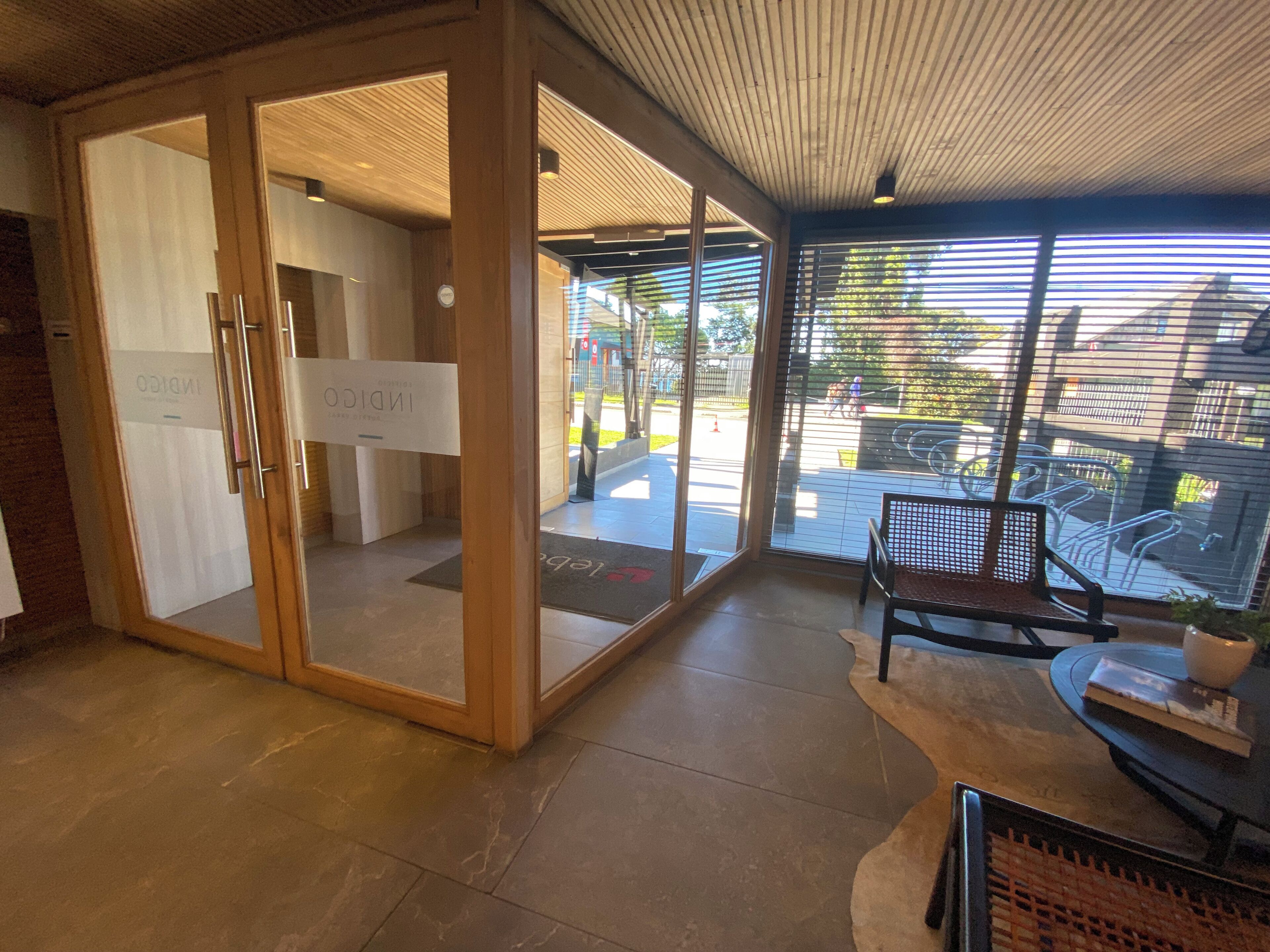 Una entrada de hotel moderna con puertas de cristal, un mostrador de recepción y un área de estar con vista a la calle.