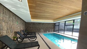 An indoor swimming pool with lounge chairs and a stone wall. - Coastal apartment with lake view, heated swimming pool and jacuzzi (Puerto Varas)