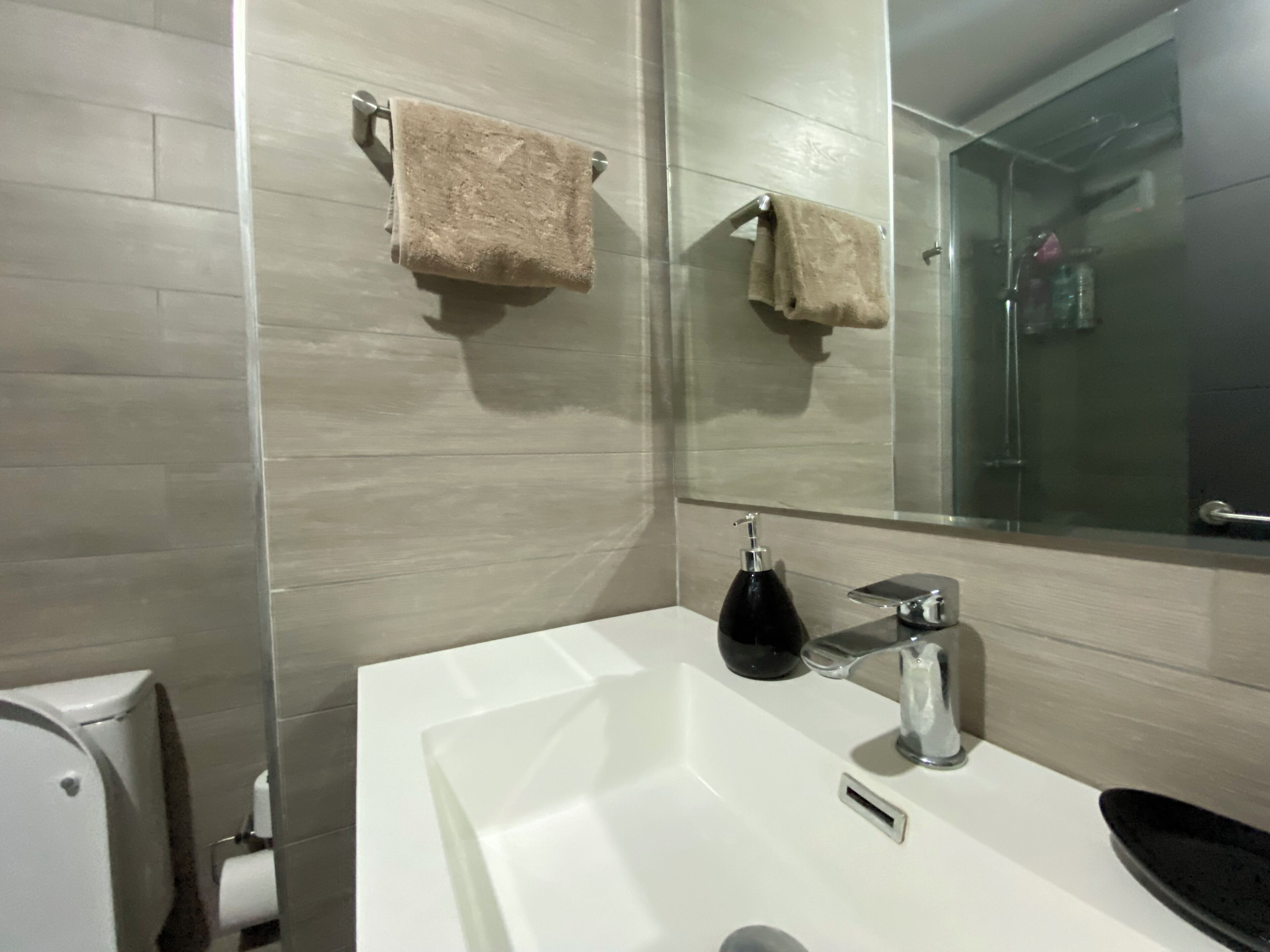 A modern bathroom with a white sink, a mirror, and two towels hanging on a towel rack.
