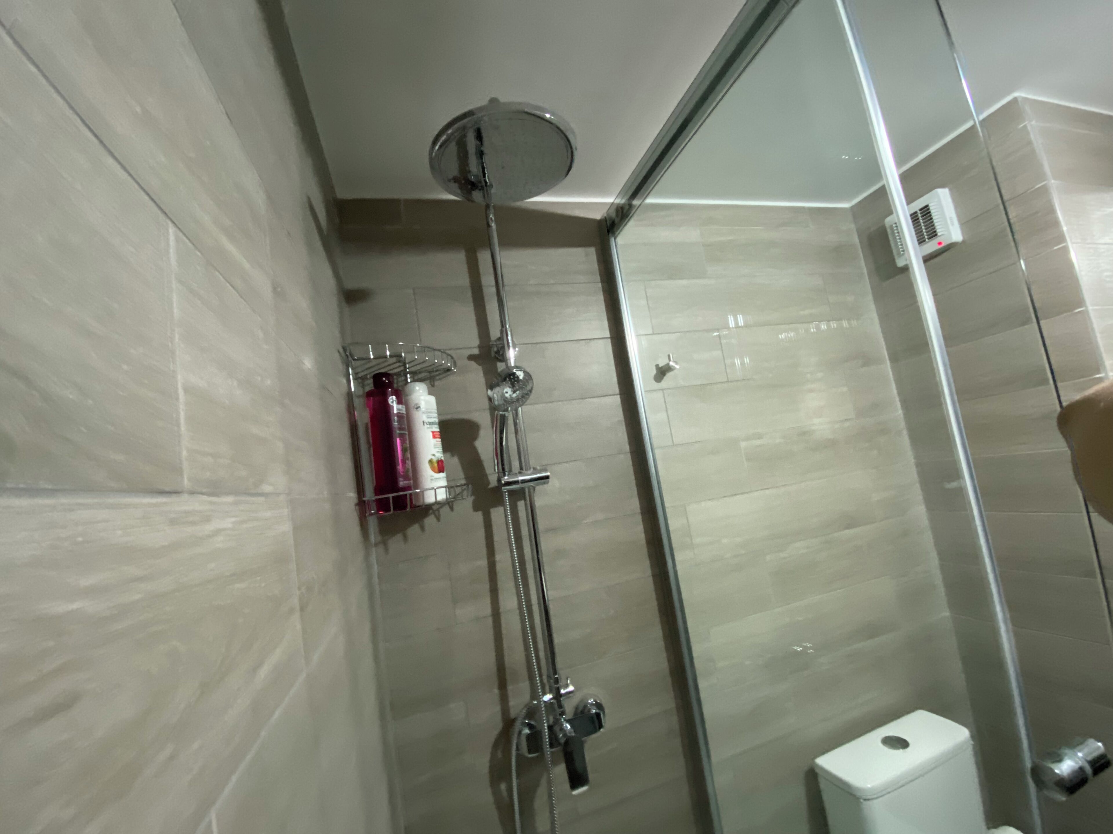 A glass-enclosed shower with a handheld showerhead and a wall-mounted faucet.