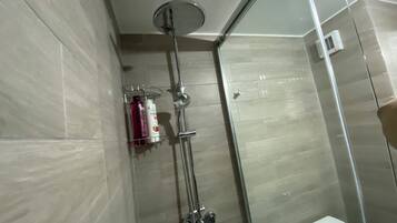 A glass-enclosed shower with a handheld showerhead and a wall-mounted faucet.