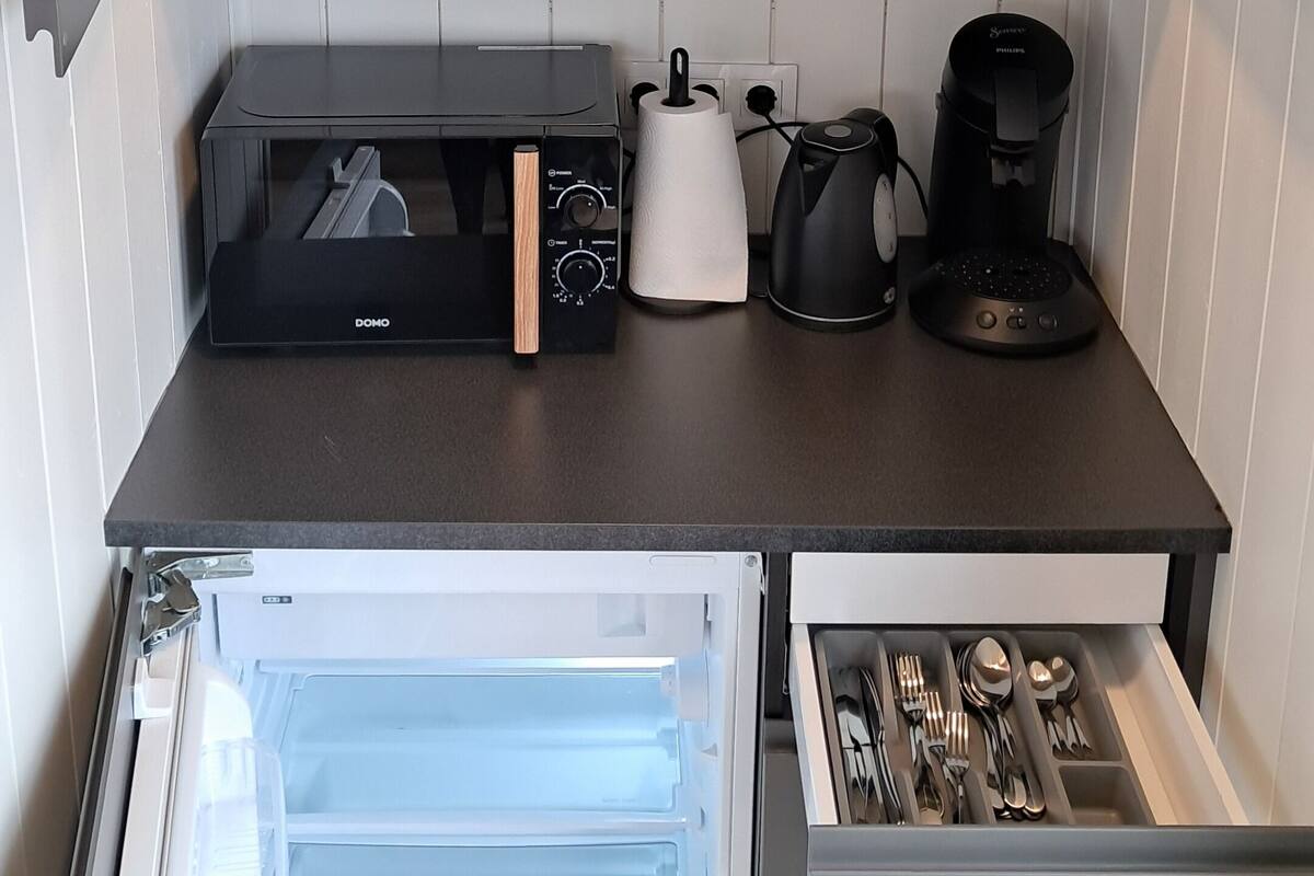 A compact kitchen with a built-in refrigerator, a coffee maker, a kettle, and a toaster.