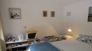 A bedroom with a bed, a bedside table with a lamp, a microwave, a kettle, and a shelf with various items. - Looking for a glamping experience with a difference? Try the Magnolia Room. (Kaipara Flats)