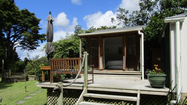 A wooden deck with a bench and a potted plant. - Looking for a glamping experience with a difference? Try the Magnolia Room. (Kaipara Flats)