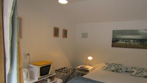 A bedroom with a bed, a nightstand, a lamp, a microwave, and a painting on the wall. - Looking for a glamping experience with a difference? Try the Magnolia Room. (Kaipara Flats)