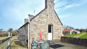 A stone building with a pitched roof, a door, and a small window. There are outdoor tables and chairs with a red umbrella. - Lovely apartment in Saint-Christophe-du-Fo (Saint-Christophe-du-Fo)