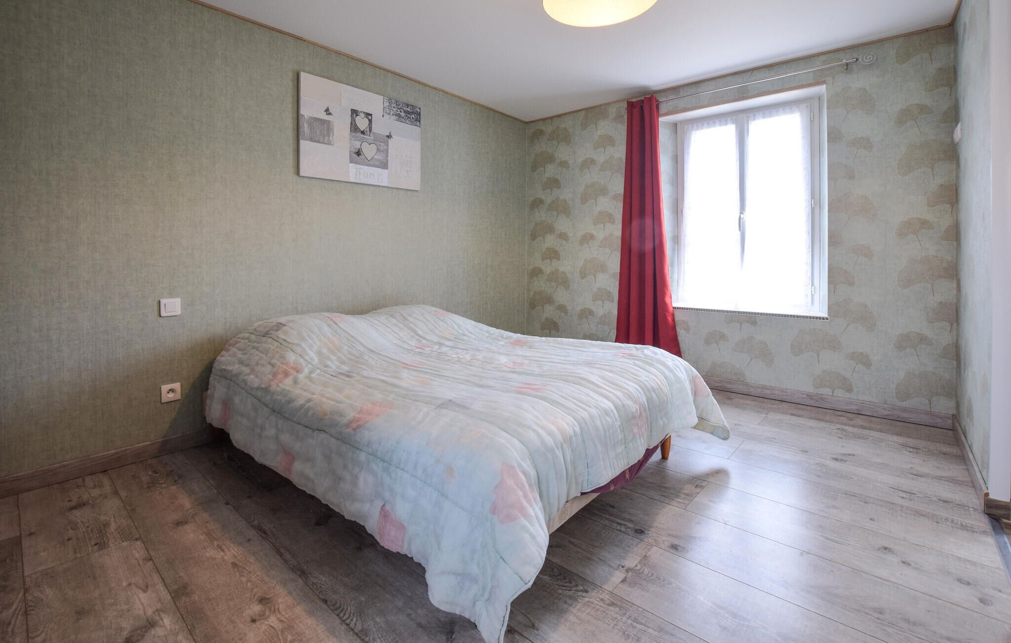 Un dormitorio con cama, ventana con cortinas rojas e imagen colgada en la pared.