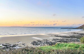A coastal landscape with a beach, rocky outcrops, and a clear sky.