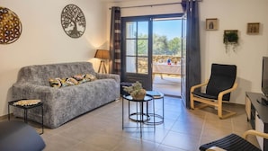 A living room with a grey sofa, a black chair, a small round table, and a TV stand. - Fiore Di Vita (Patrimonio)