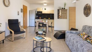 A modern living room with a sofa, a chair, a small table, and a kitchen area in the background. - Fiore Di Vita (Patrimonio)
