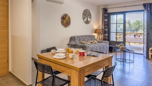 A dining area with a wooden table, black chairs, and a grey sofa. There are decorative wall art pieces and a window with curtains. - Fiore Di Vita (Patrimonio)