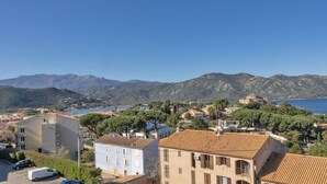Un pueblo costero con edificios, cielo azul despejado y montañas al fondo.