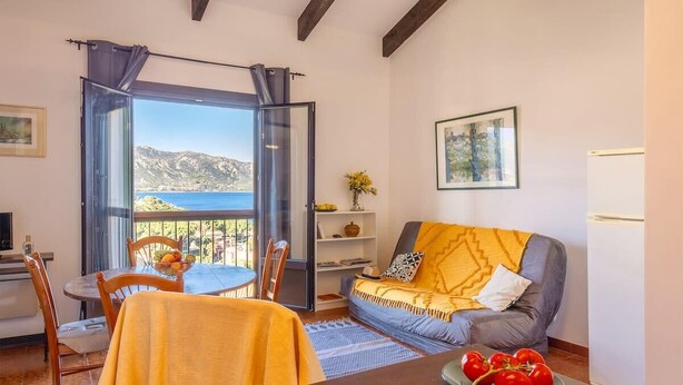 Una sala de estar acogedora con comedor, un sofá con una manta amarilla y vistas al mar.