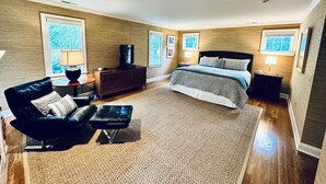 Ein geräumiges Schlafzimmer mit einem großen Bett, einer Sitzecke mit Sessel und Hocker, einem Schminktisch und einem Fernseher.